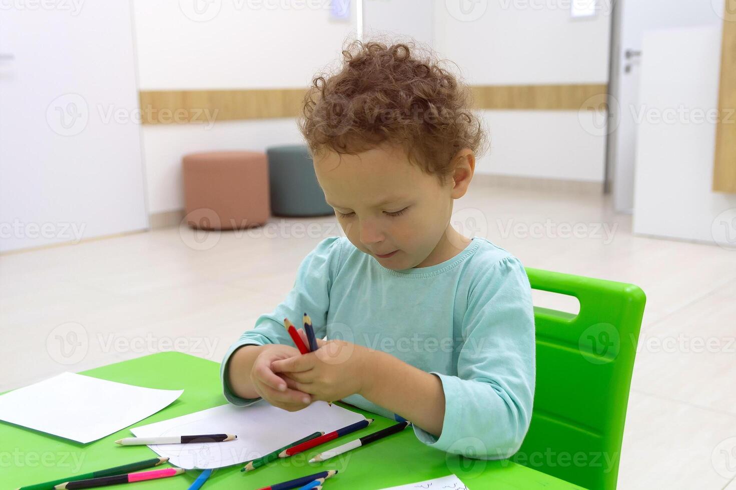 Cute child draws with pencils sitting at the table. People photo