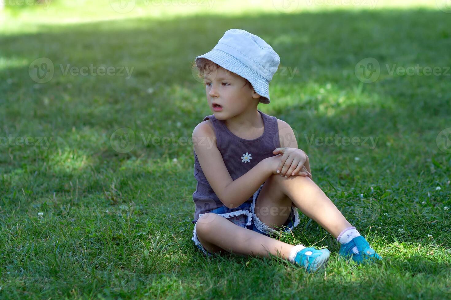A child in a panama hat sits on the grass in the park photo