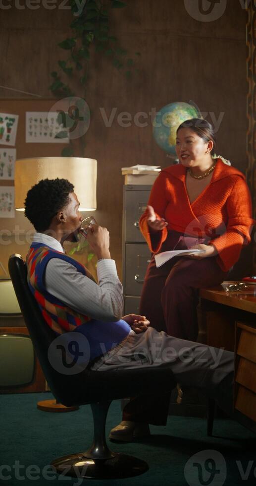 A man is talking to his colleague and drinking coffee sitting in a retro office. photo