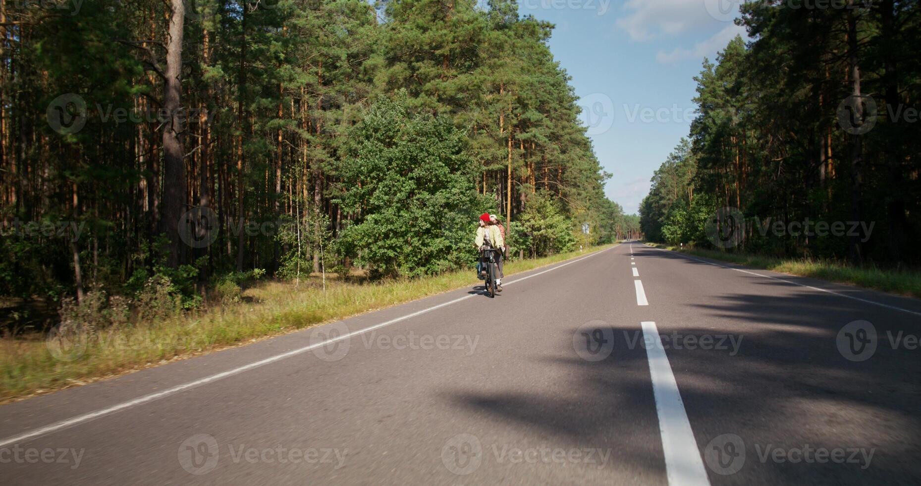 A young couple is riding a bike on a road in the middle of the forest. Active leisure photo