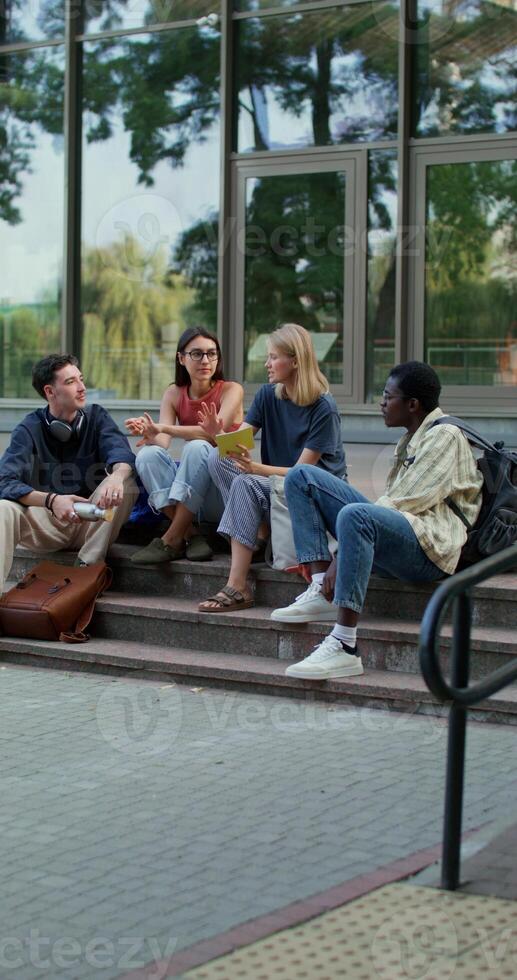 A group of young people are talking while repeating lessons sitting on the university steps. Sunny summer day photo