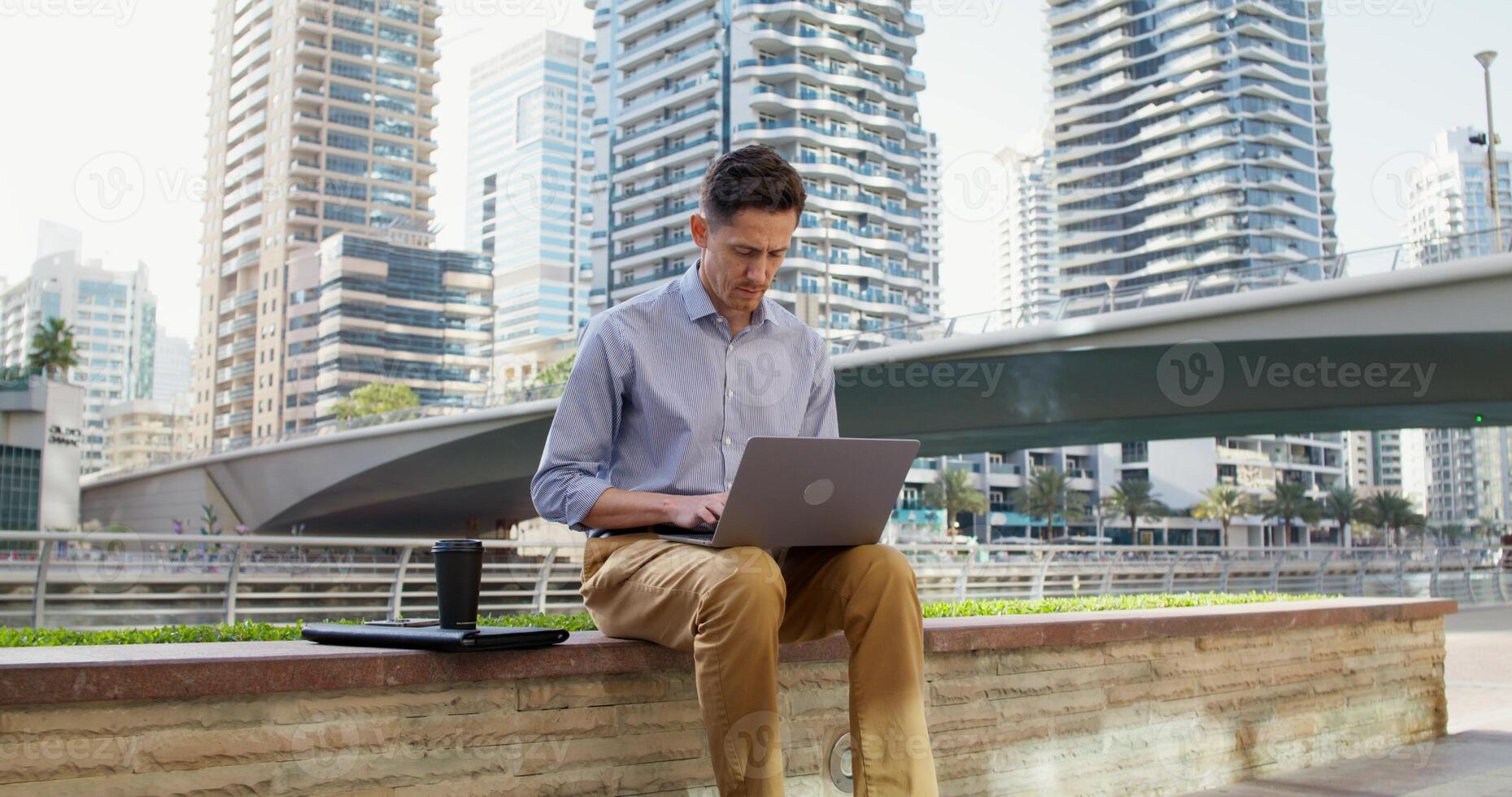 A serious man works remotely while sitting on a city street in a modern metropolis. photo