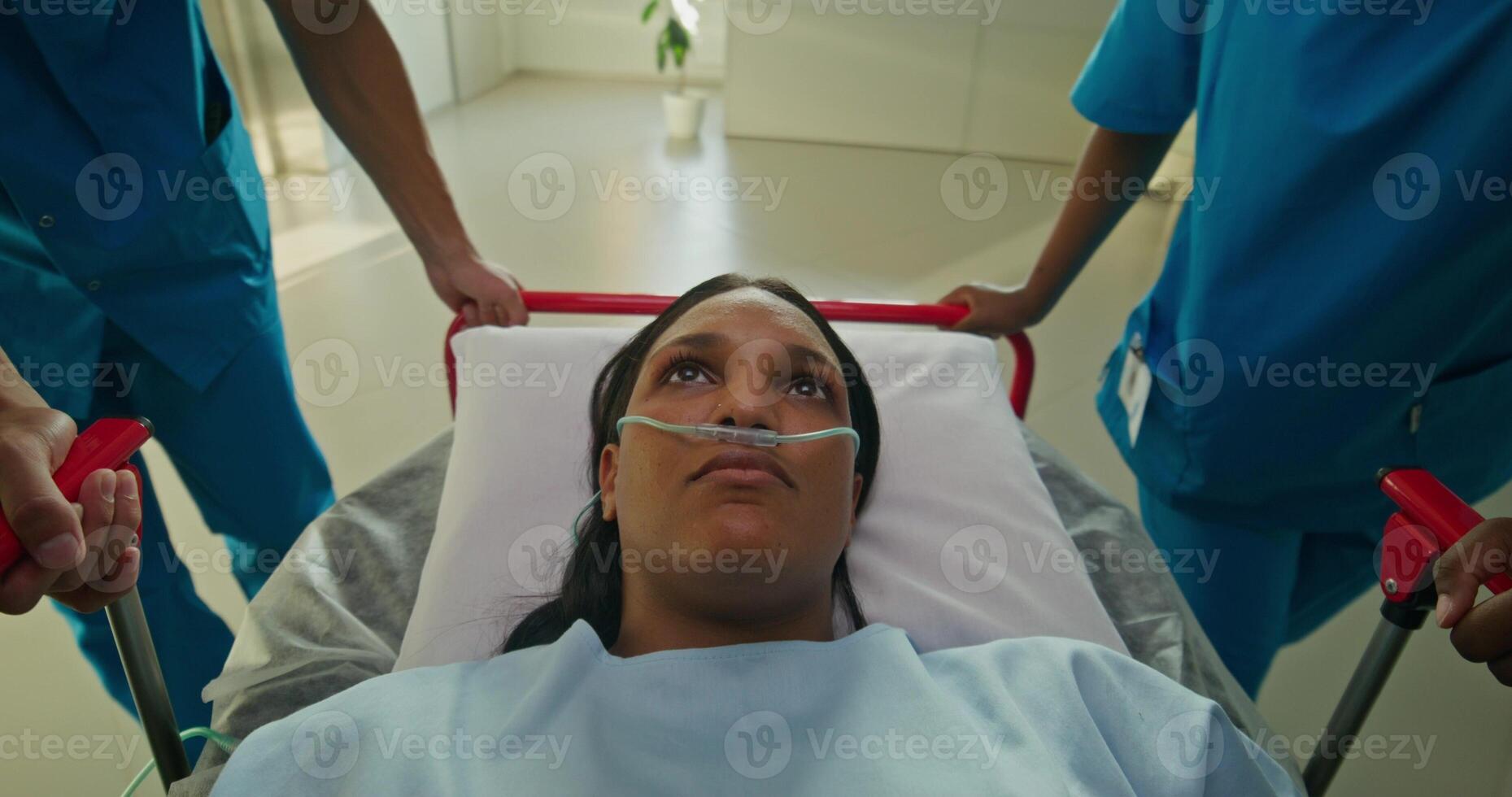 A woman with a breathing tube in her nose is lying on a gurney. She is being driven down the hospital corridor photo