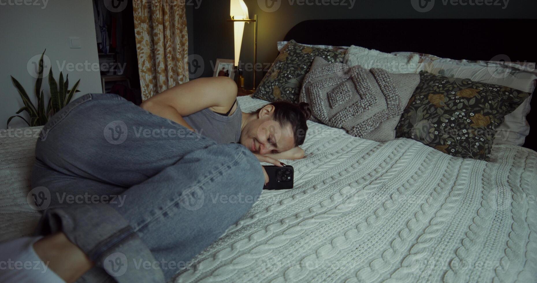 A woman cries when she uses a mobile phone. She's lying on the bed at home photo