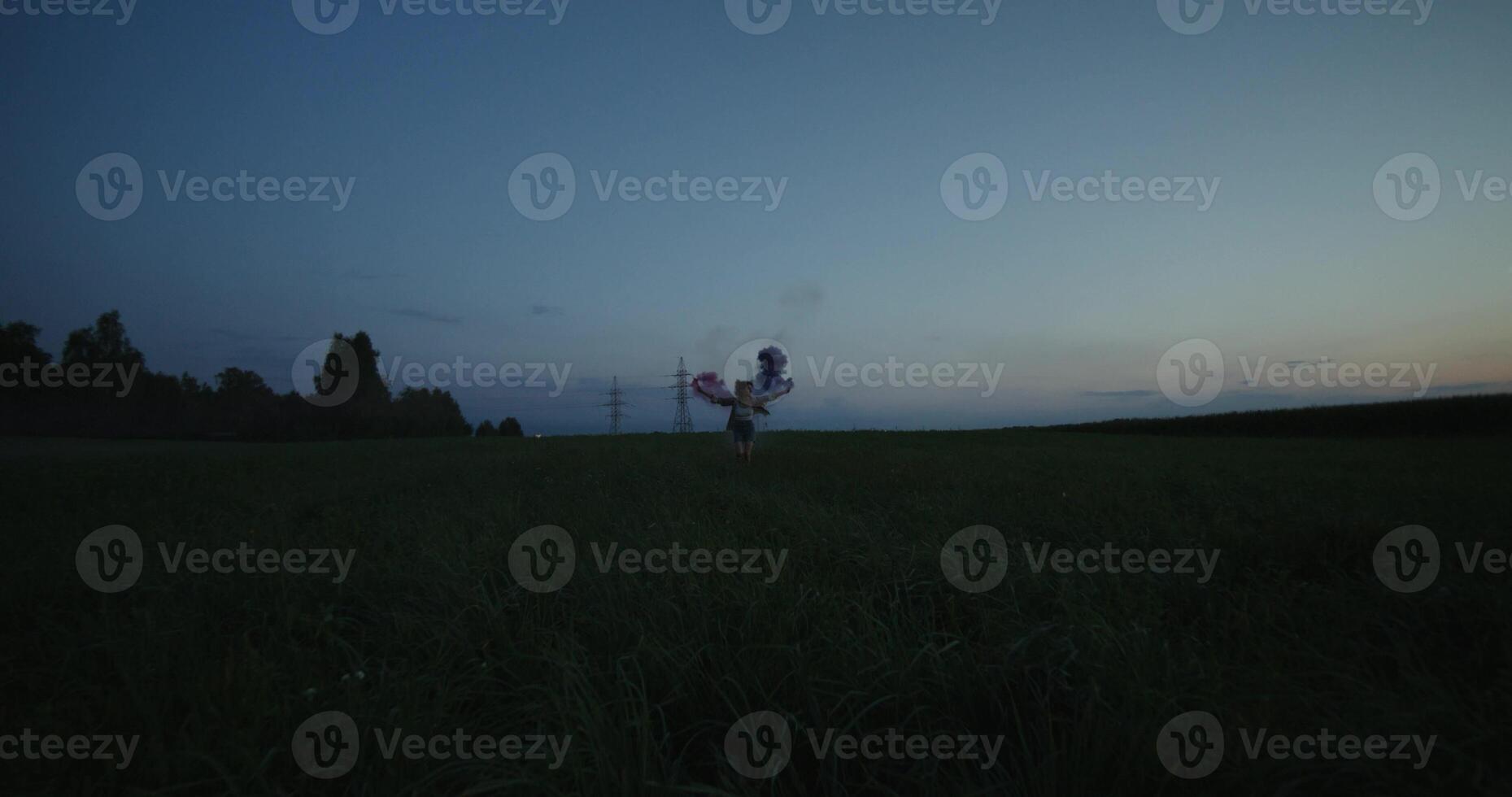 A young woman blows pink and blue smoke running across a field photo