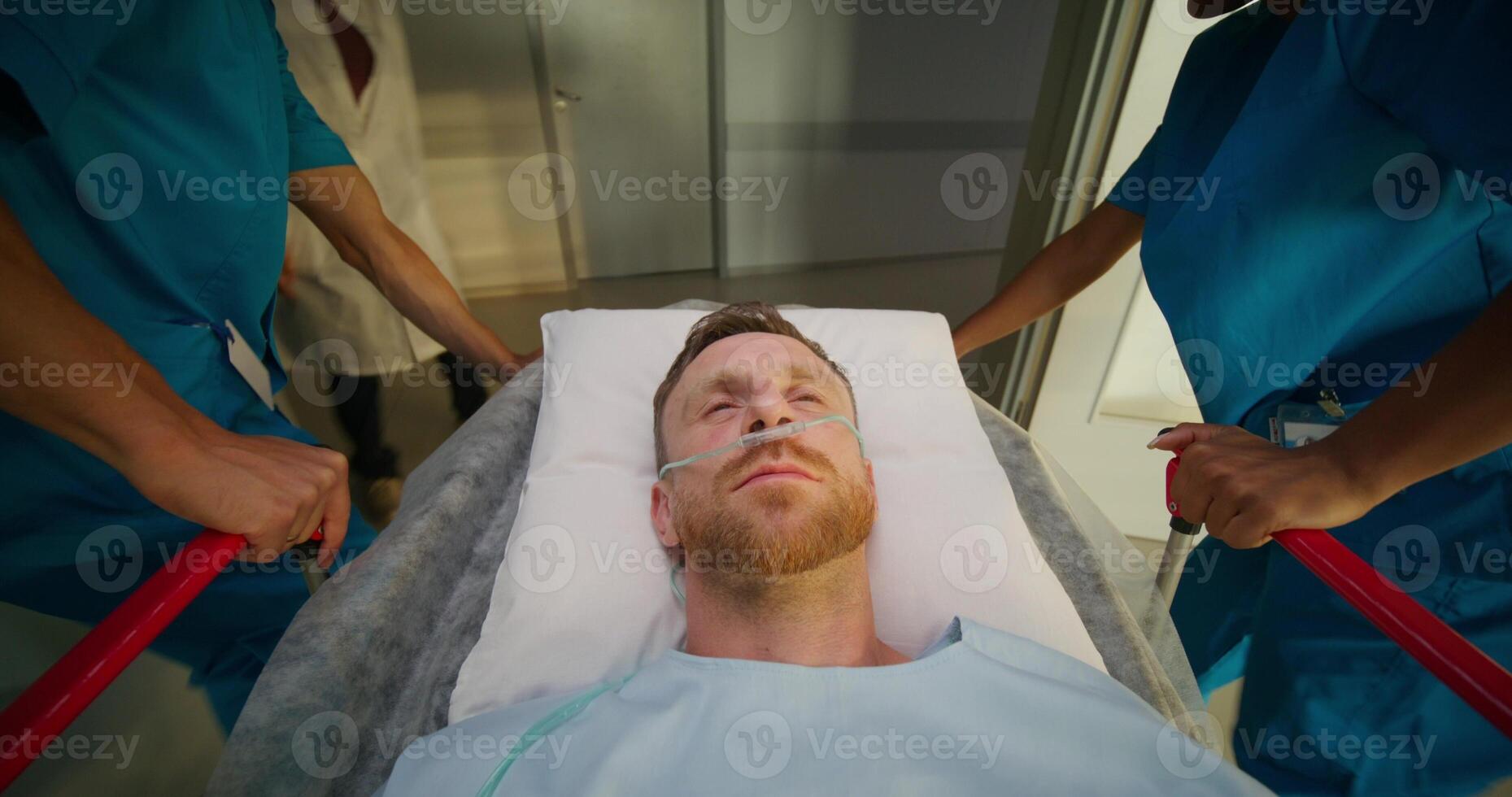 A man is lying on a medical gurney, he is being taken through the hospital corridor. The oxygen tube photo