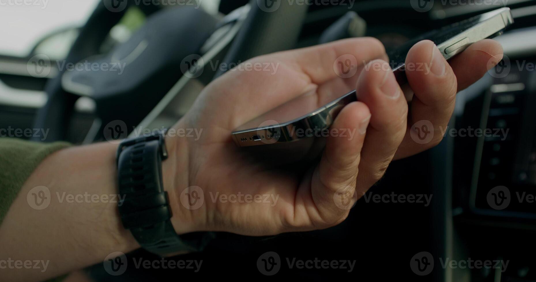 A man connects a mobile phone with a cable to a car while sitting in the driver's seat. Close-up of his hands photo
