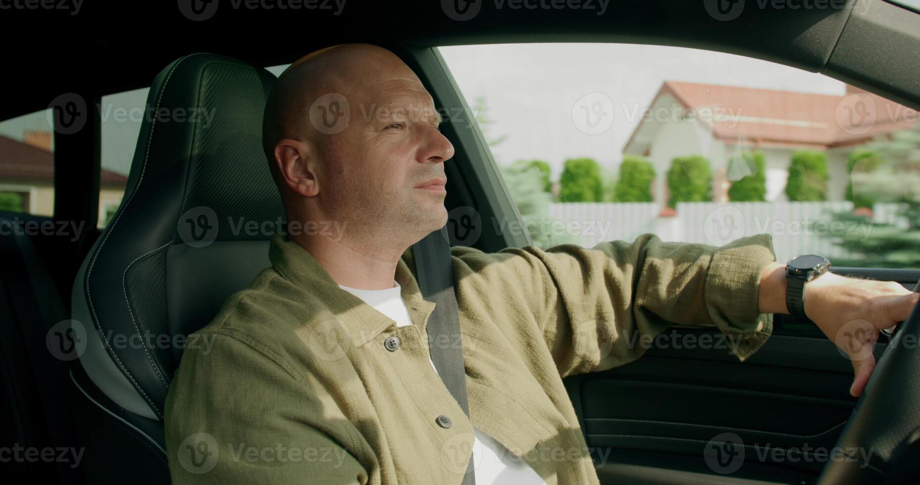 A man wearing a seat belt drives a car with a calm look. View from the car interior. Summer photo