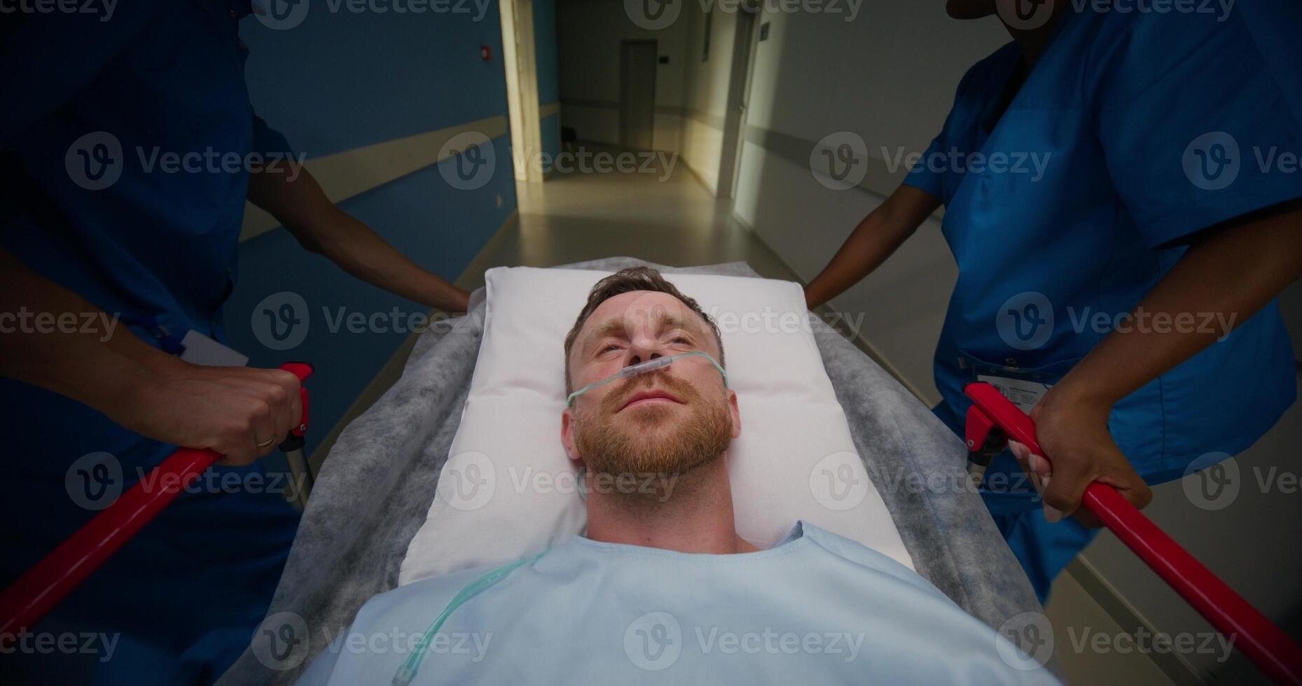 A man is lying on a medical gurney, he is being taken through the hospital corridor. The oxygen tube is in his nose photo