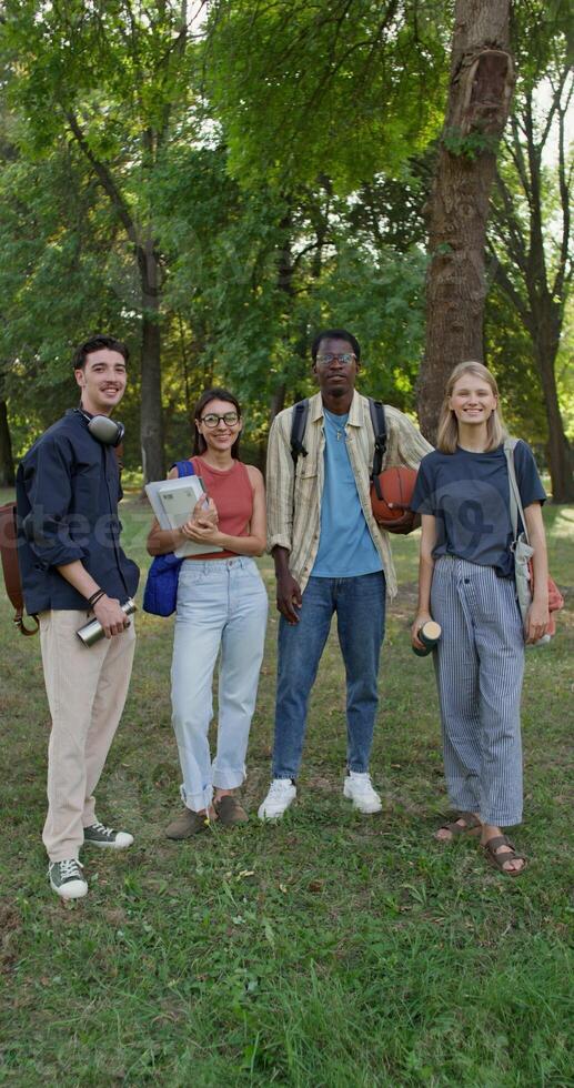 A group of young people with briefcases on their shoulders are smiling at the camera while standing in a city park. photo