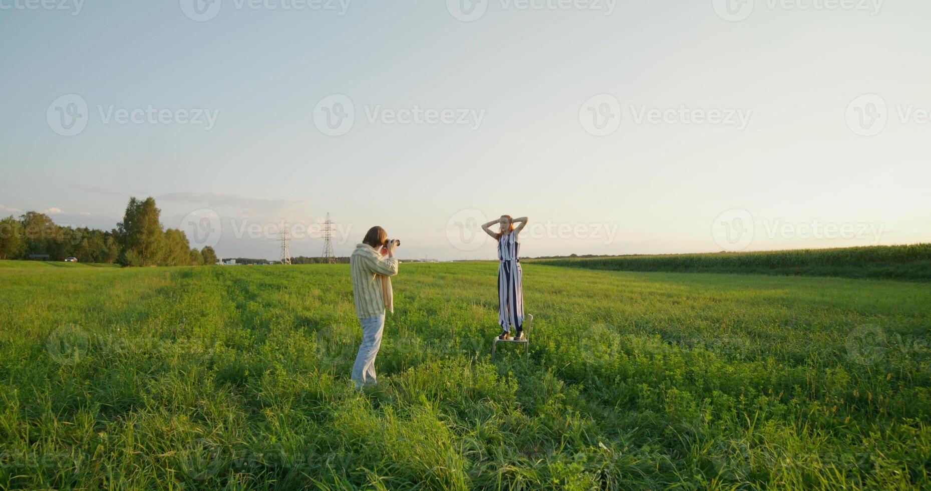 A man takes pictures of a young woman at sunset in a field. photo
