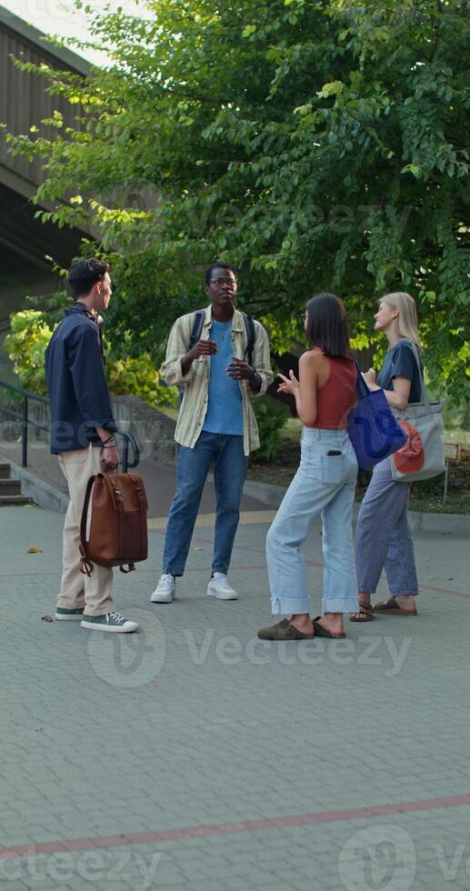 A group of young people with bags and backpacks are talking and smiling standing near the university. photo