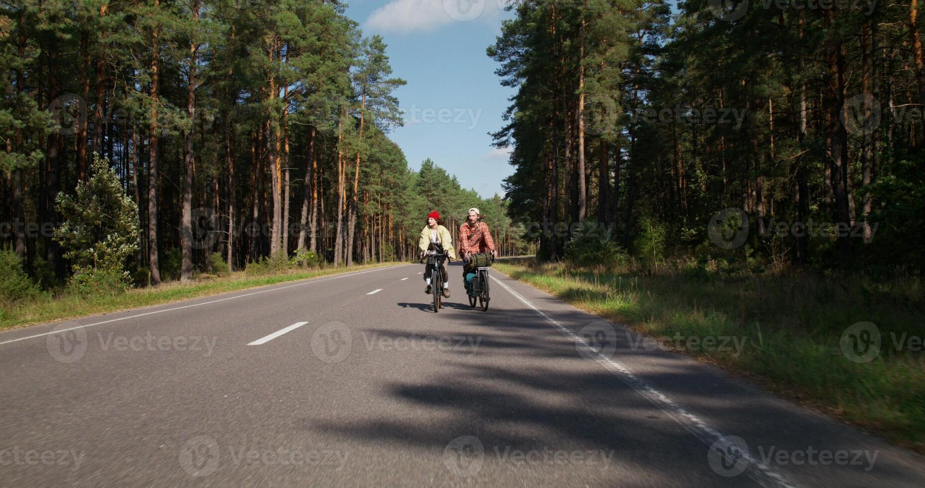 A man and a woman ride bicycles in the middle of a road surrounded by forest. Active leisure on a sunny day photo