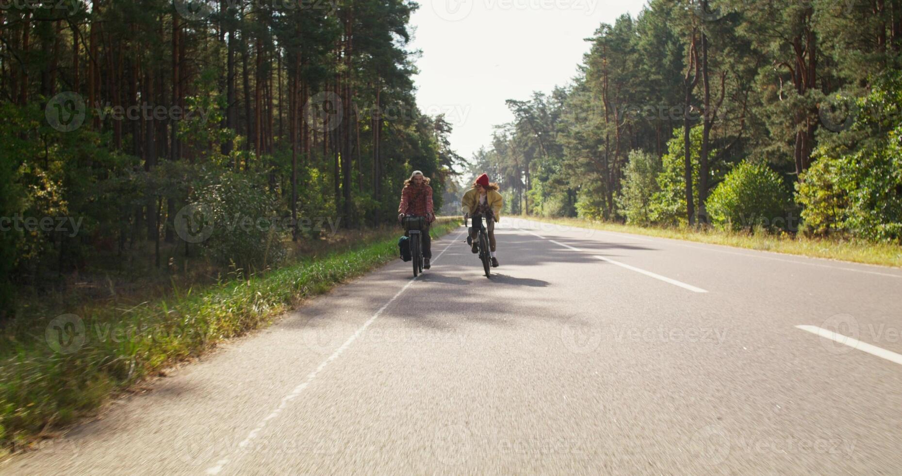 A man and a woman ride bicycles on an asphalt road surrounded by forest. A sunny day photo
