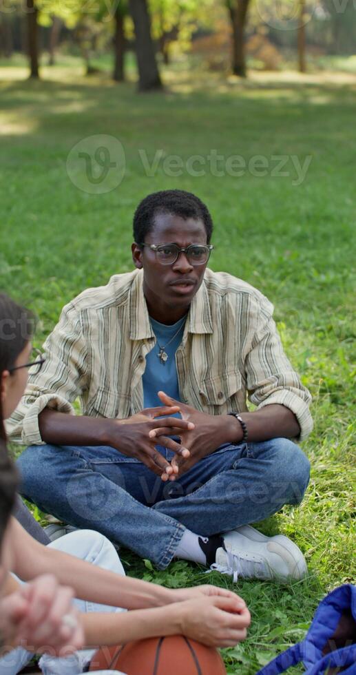 A man is talking to his friends while sitting on the grass in the park. Sunny summer day photo