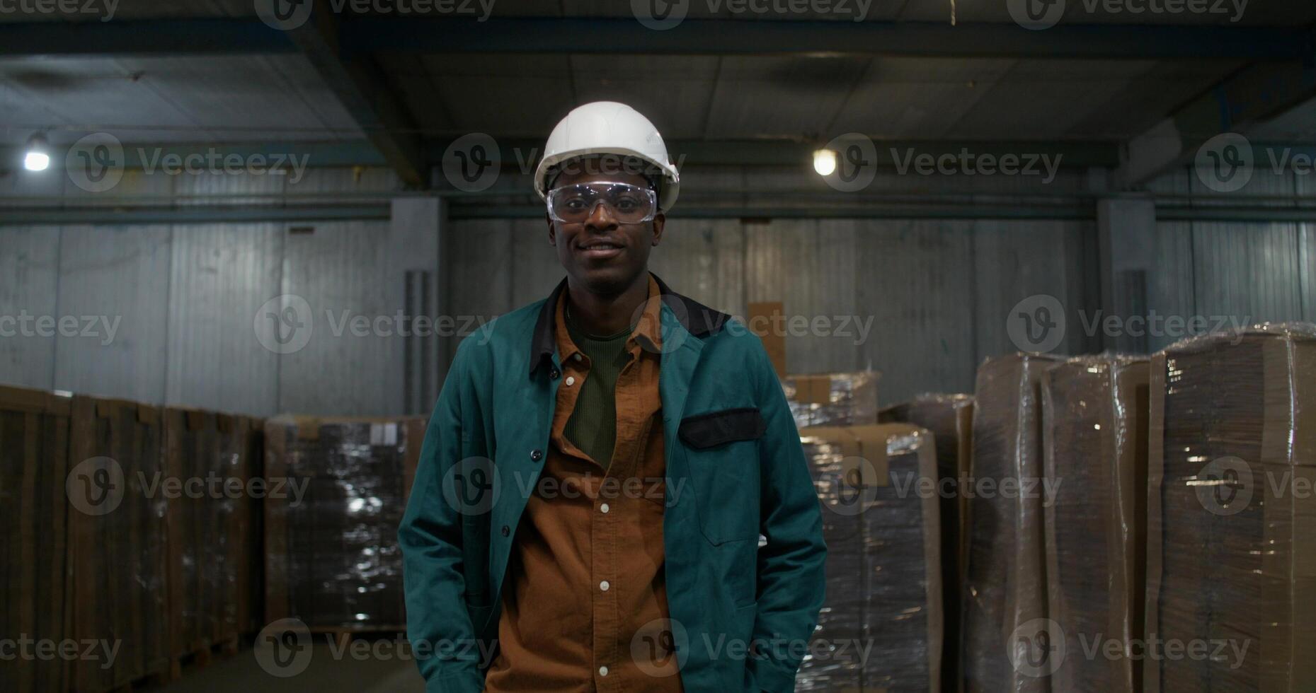 A man in a work uniform is smiling at the camera. He is in the factory warehouse. photo
