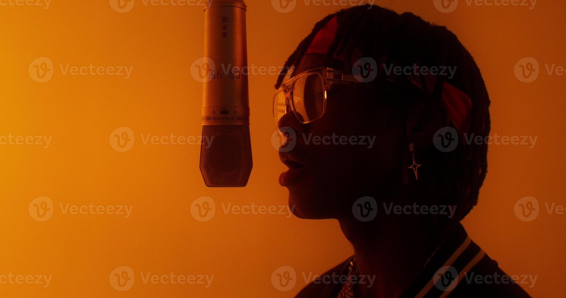 A stylish young man sings into a hanging microphone. Studio in orange light. Close-up of his face photo