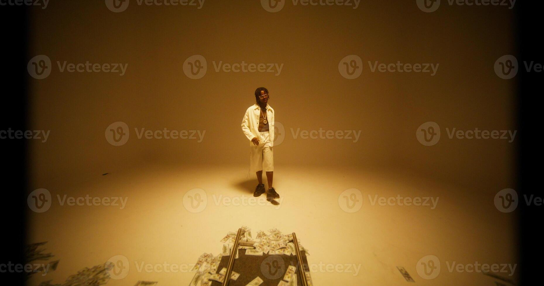 A man sings and dances in the yellow light of the studio. Dollar bills on the floor in front of him photo
