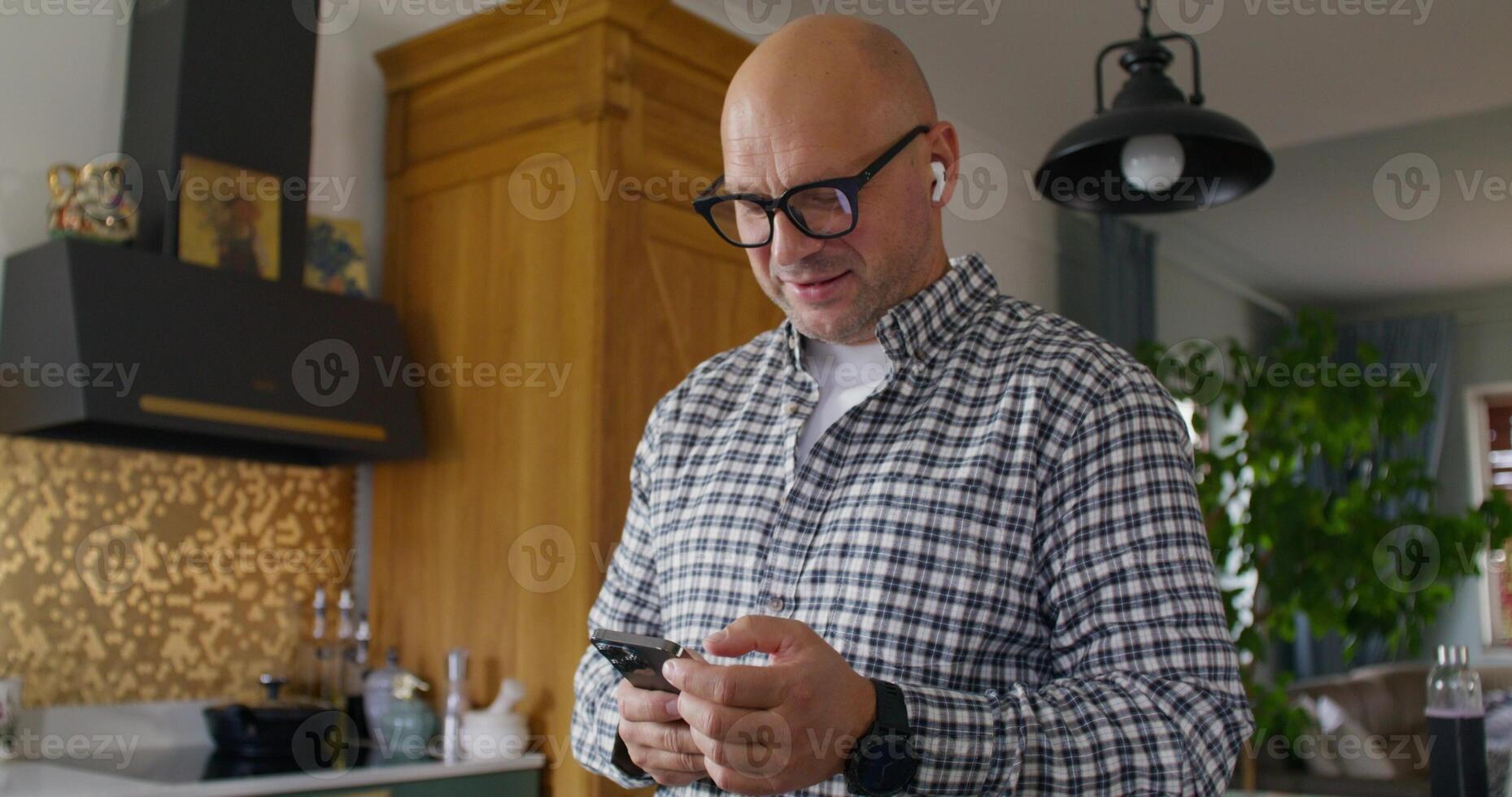 A man with earbuds in his ears is talking on a mobile phone. He holds the phone in his hands. photo