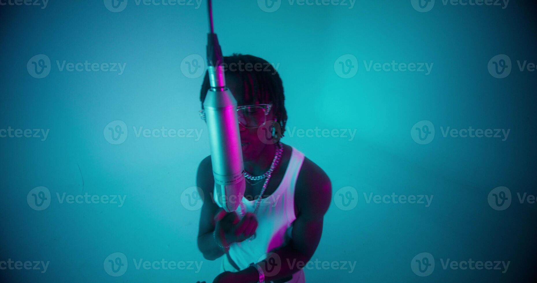 An African-American man with dreadlocks sings into a microphone. Studio photo