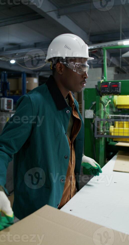 A man works in a paper mill. He talks to his colleague as he stacks the sliced cardboard photo