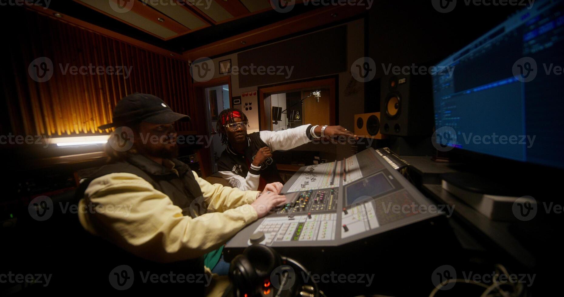A sound engineer and a singer are discussing a recorded song in a studio. They are sitting in front of an audio mixer photo