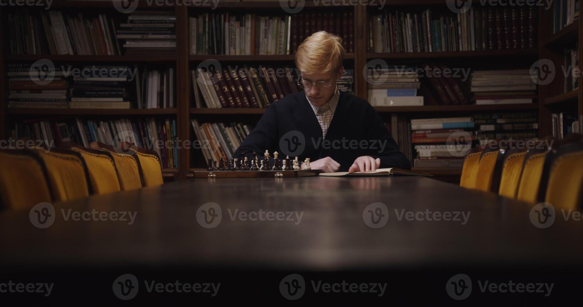A young man of European appearance, dressed in a business suit, is studying with concentration to play chess alone, using a textbook photo