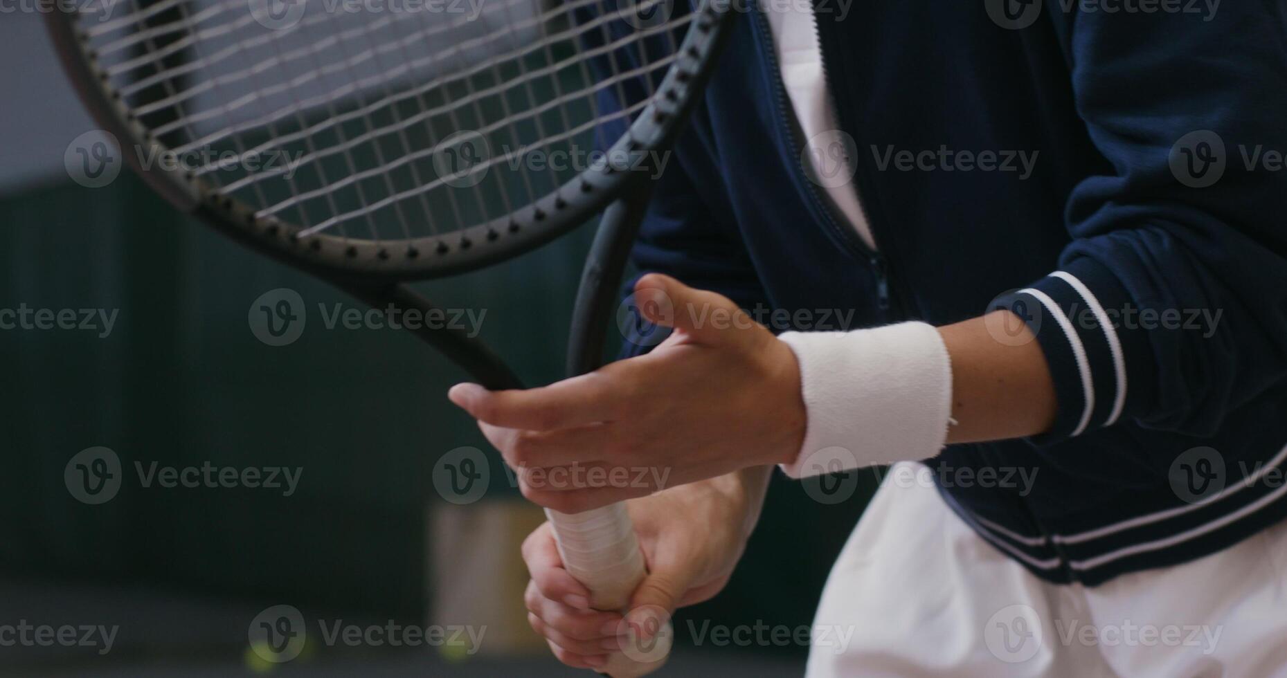 A young beautiful red-haired woman tennis player is intently waiting for a pass from an opponent, twirling the racket in her hands and getting ready to hit. Tennis match on the indoor tennis court photo