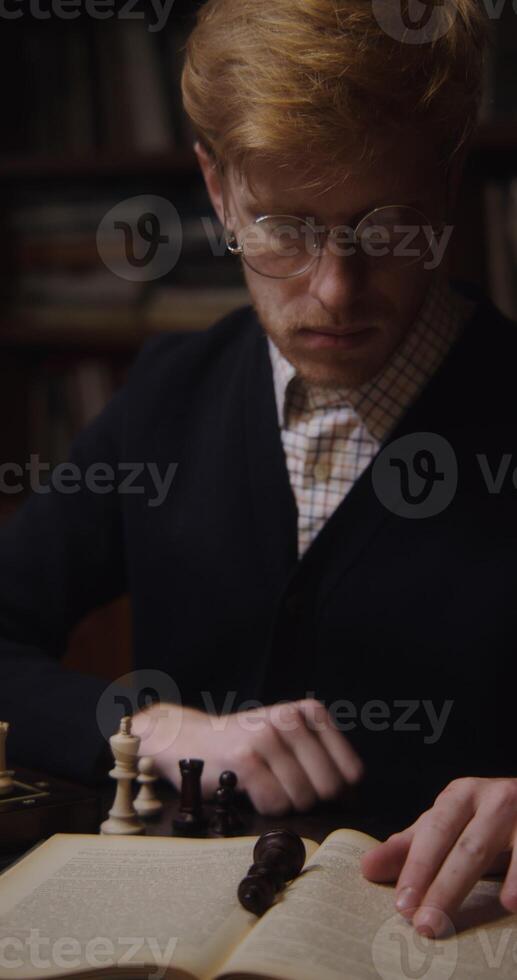 A young man of European appearance, dressed in a business suit, is studying with concentration to play chess alone photo
