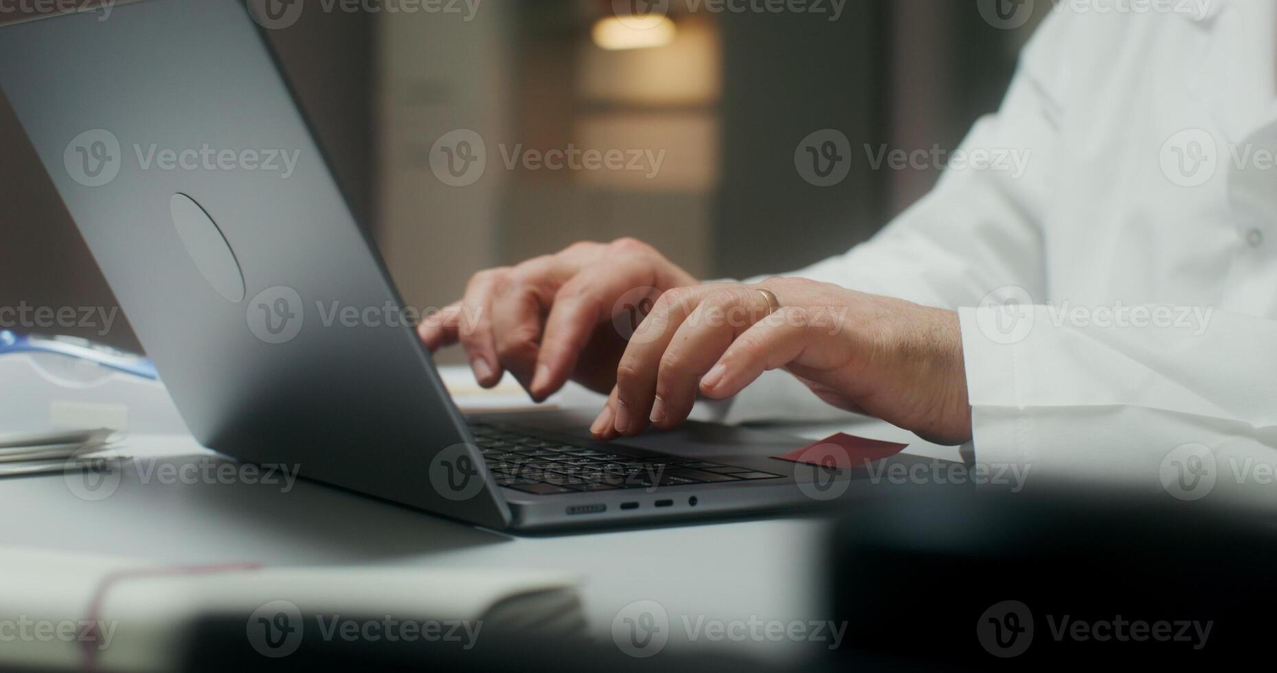 The doctor is typing on a laptop sitting at a table in a medical office, working in a clinic. Close-up of his hands photo