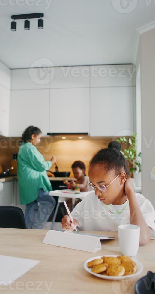 A girl draws with a stylus on a tablet while sitting at the kitchen table at home. photo