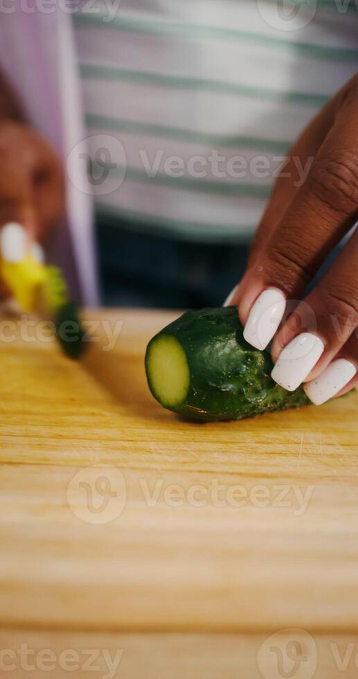 Women's hands are cutting a cucumber while preparing a salad in the kitchen, there is no face - cutting photo