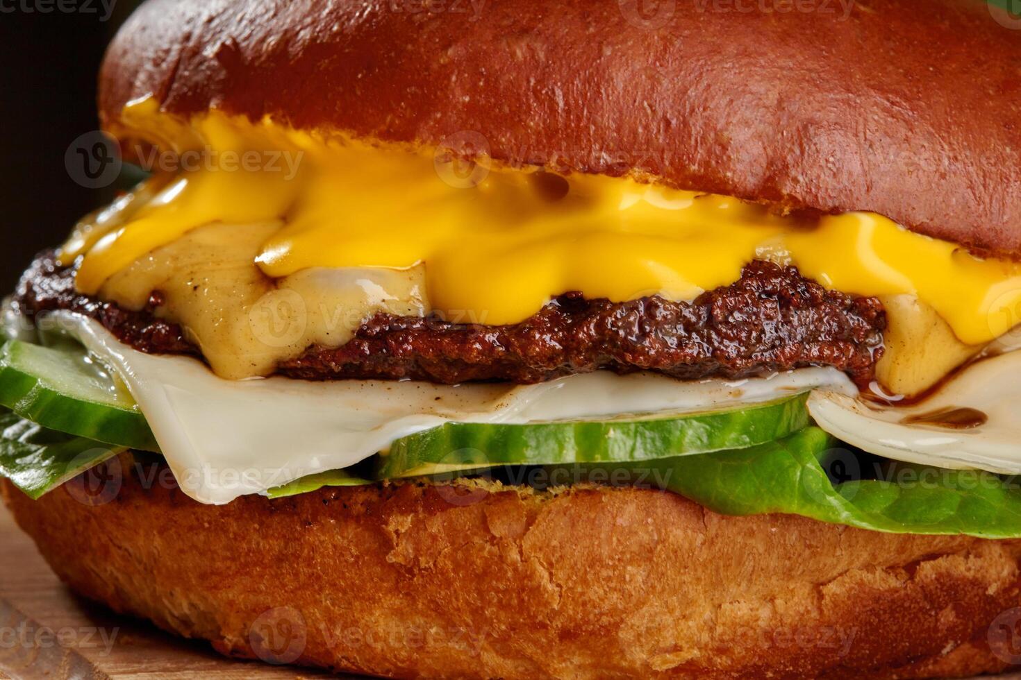 Delicious cheeseburger dripping with melted cheddar cheese, pickles, and lettuce on brioche bun photo