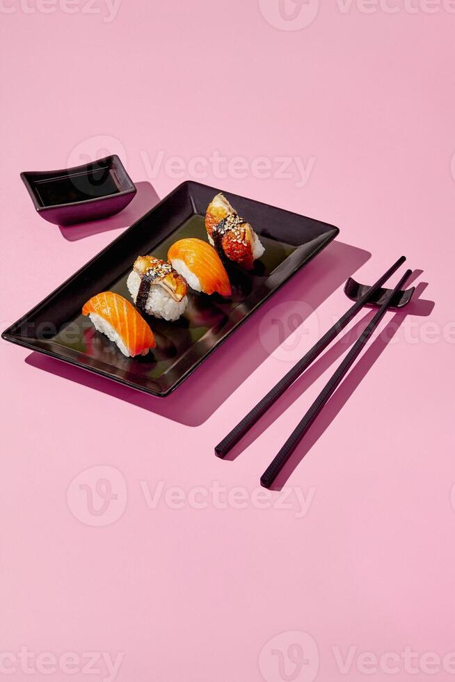 Delicious sushi pieces with soy sauce and chopsticks on pink background photo