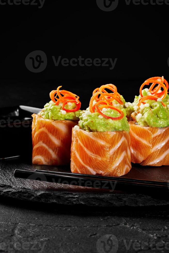 Delicious salmon sushi rolls topped with guacamole and carrot garnish on black background photo
