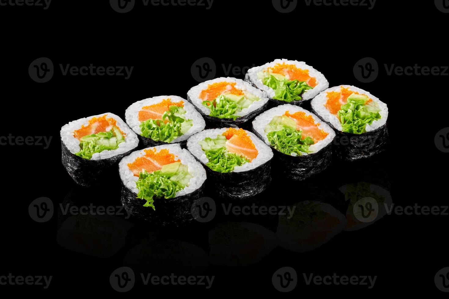 Sushi rolls with salmon, avocado, salad and fish eggs reflecting on black background photo