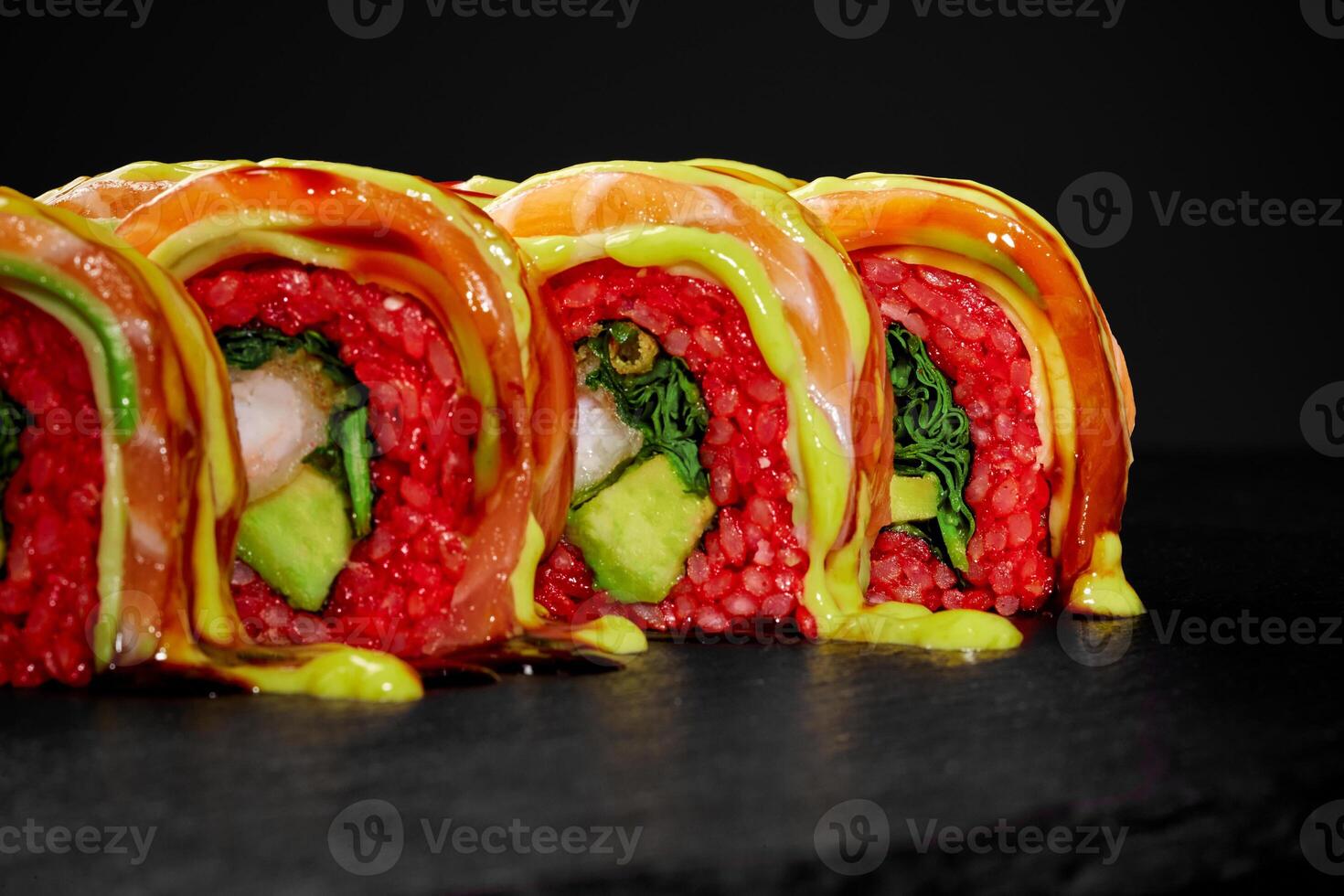 Uramaki sushi rolls with salmon, avocado, and red rice drizzled with sauce on a black background photo