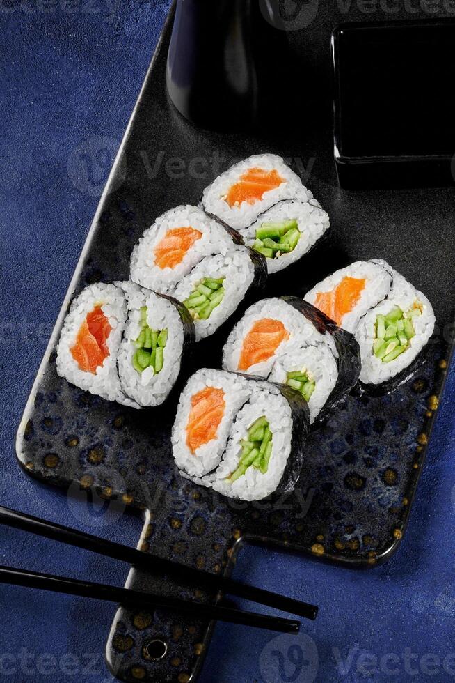 Delicious uramaki sushi rolls with salmon, cucumber, and soy sauce being served on a tray photo