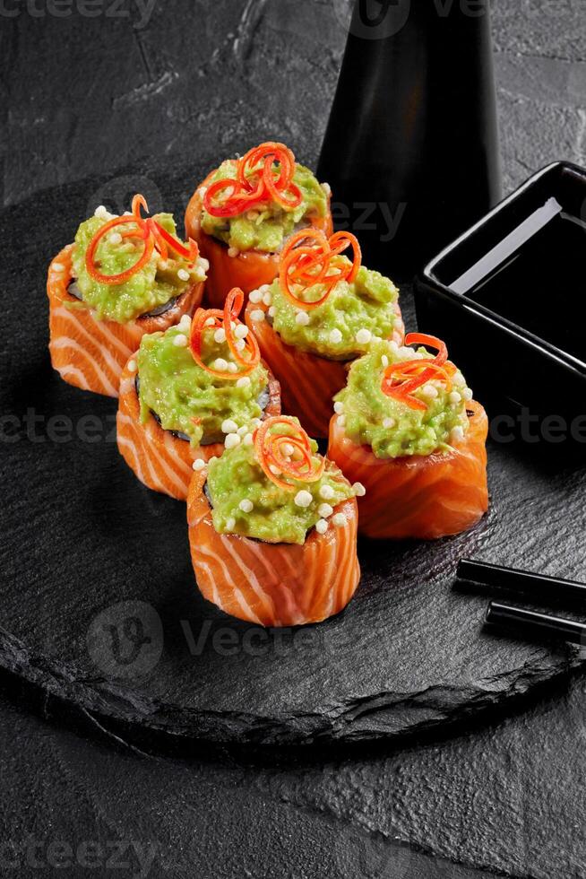 Uramaki sushi rolls with salmon, avocado, tobiko roe, and chili threads on black slate photo
