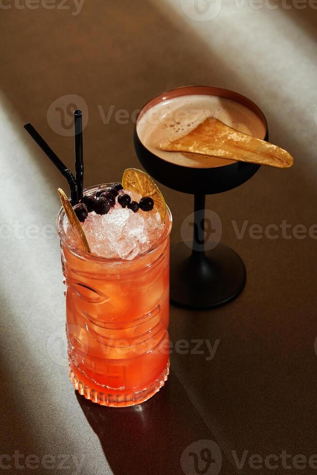 Two refreshing cocktails with fruit and ice sitting on bar photo