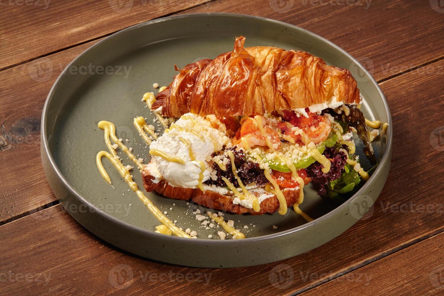 Delicious croissant sandwich with shrimps, avocado, and salad on a plate photo