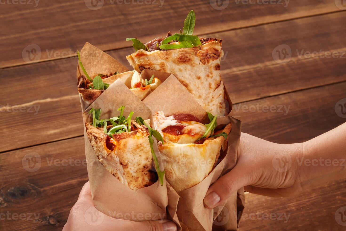 Hands holding pizza wraps with arugula on rustic wooden table photo