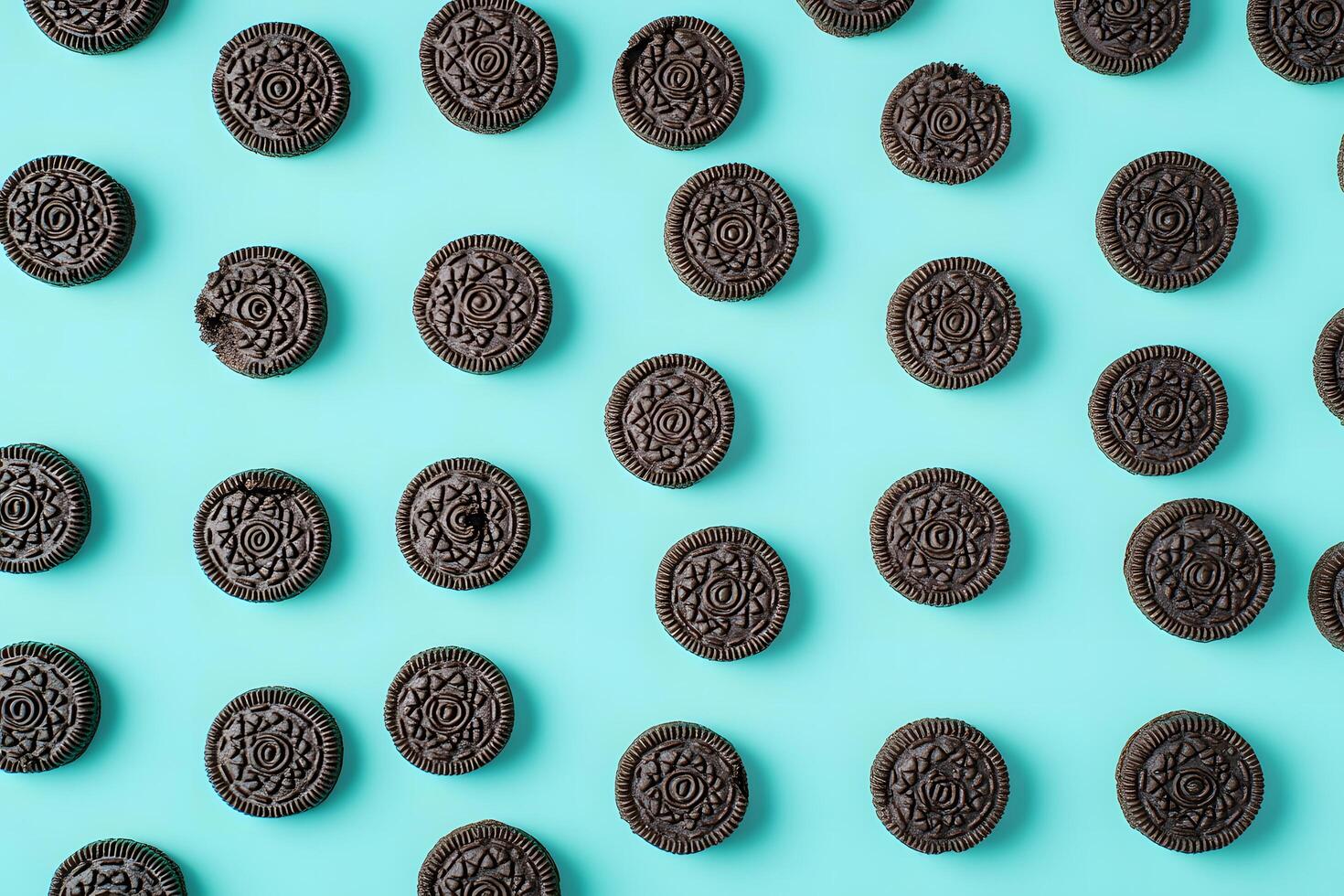 Brown sandwich cookies are meticulously arranged against a turquoise background, with one cookie partially eaten photo