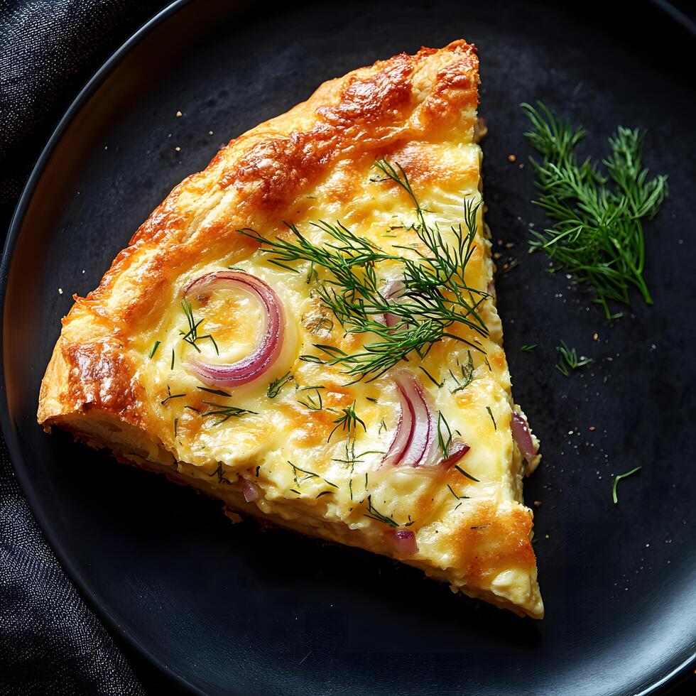Single slice of quiche with red onions and dill sits on dark plate photo