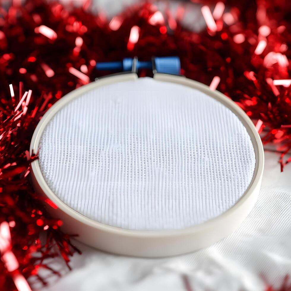 Embroidery hoop displays white canvas nested within festive red tinsel for craft preparation photo