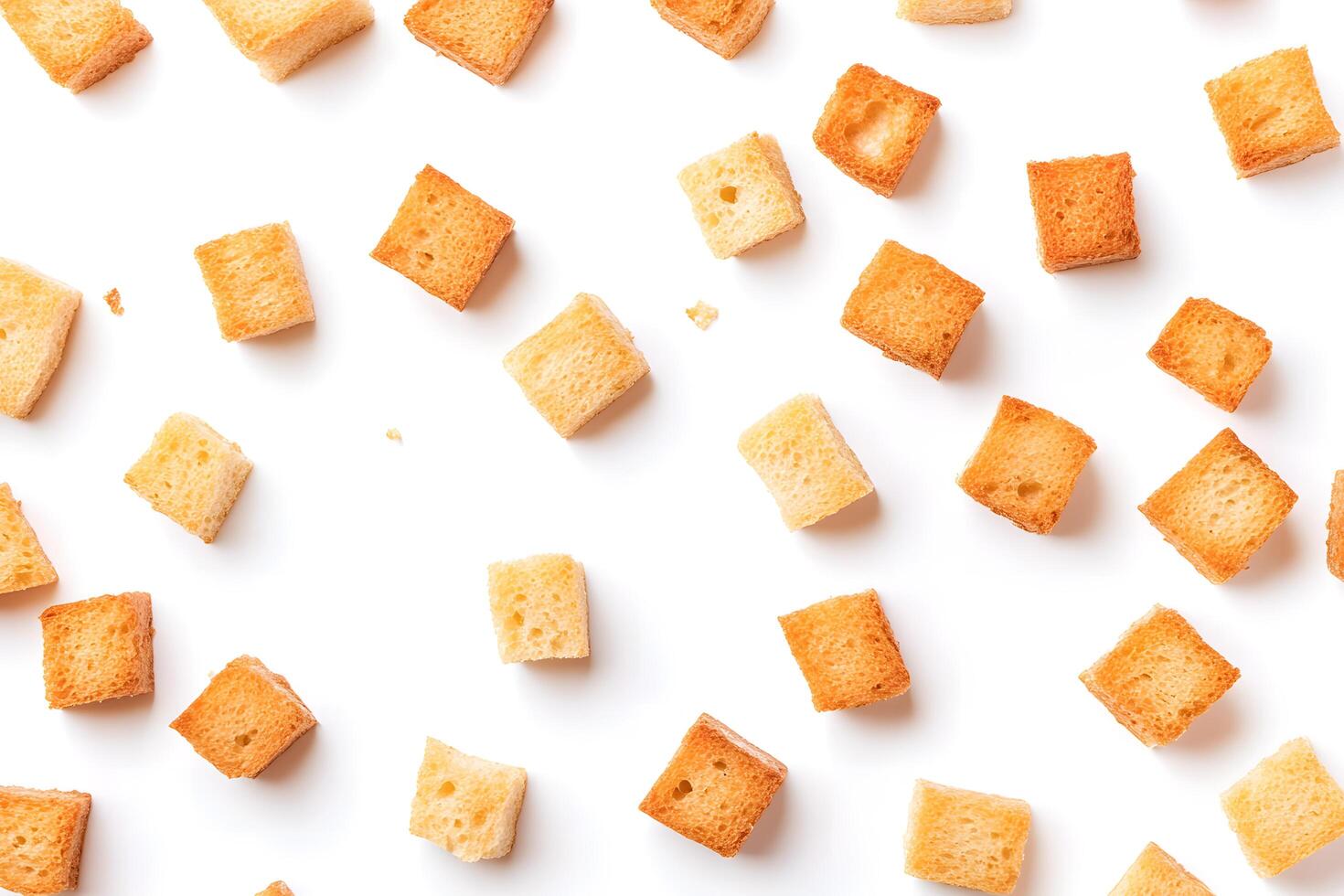 Multiple golden brown croutons are scattered evenly on a bright white surface, simple and plain photo