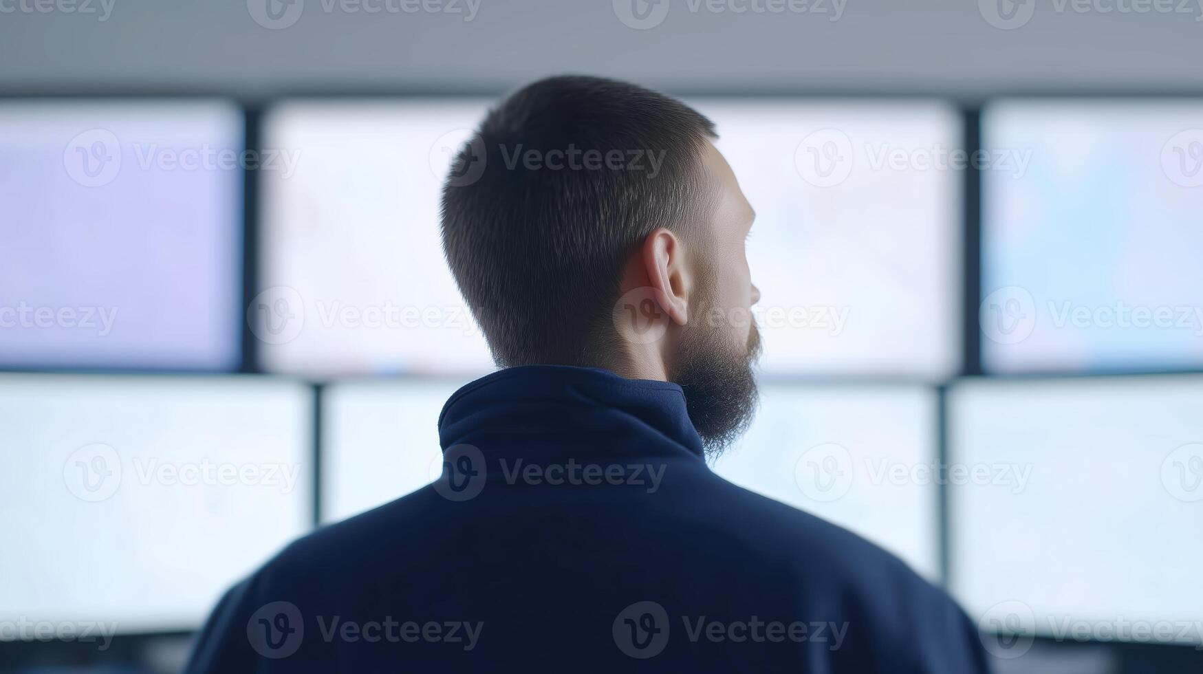 Male professional with beard is observing multiple computer screens in a modern workspace with a focus on technology and data analysis photo