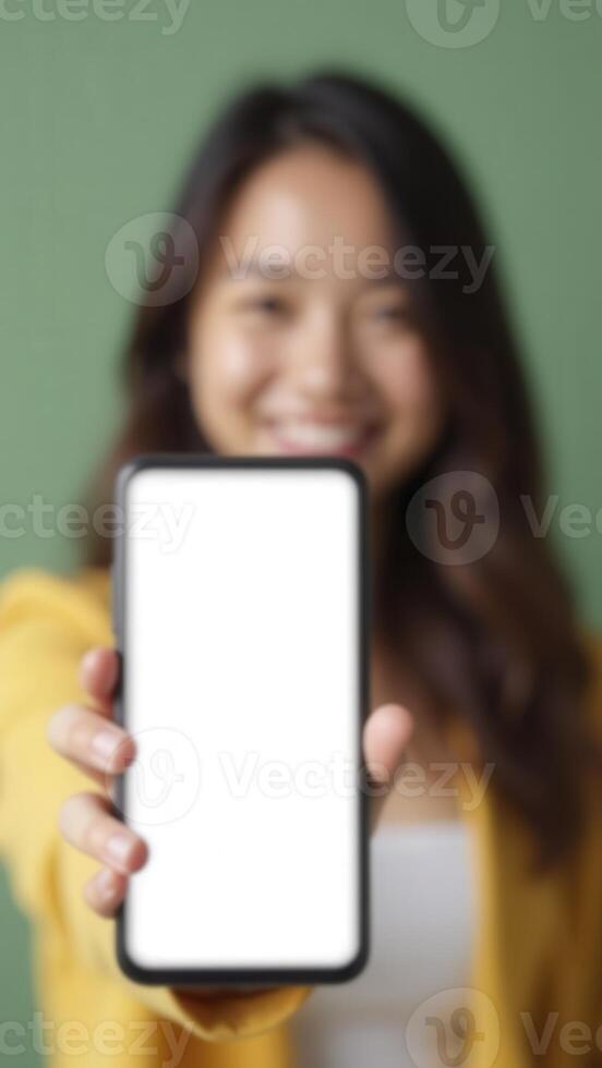 Smiling woman showing smartphone with blank white screen on green background photo