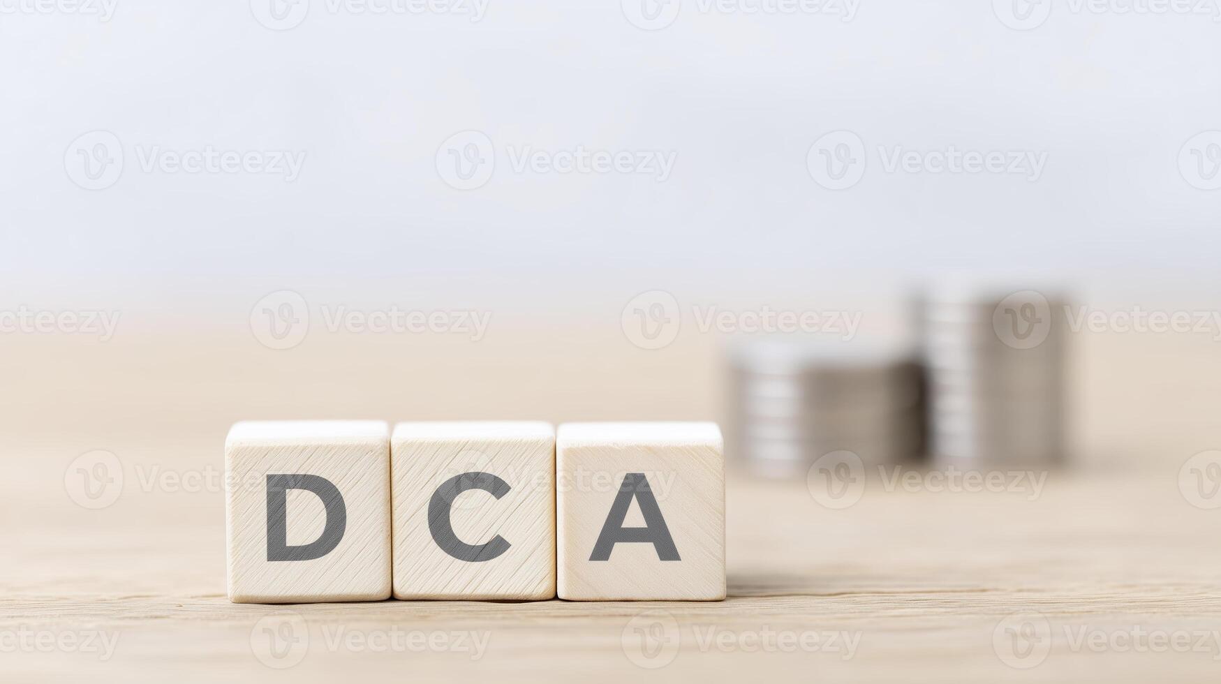 Wooden blocks displaying letters DCA are placed on a wooden surface, with stacks of coins in the background, symbolizing investment strategies and financial planning concepts photo
