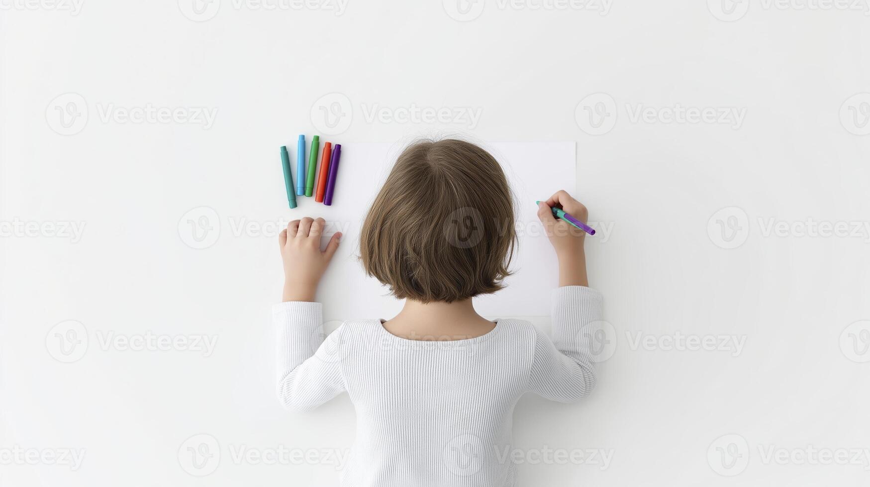Child with short brown hair is drawing on a blank sheet of paper, surrounded by colorful markers, showcasing creativity and artistic expression in a minimalistic environment photo
